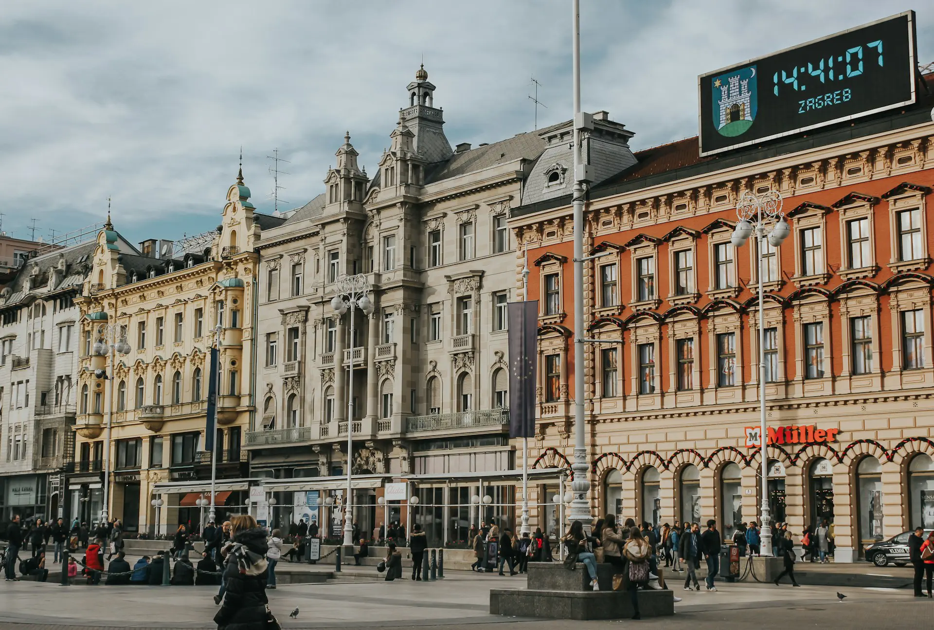 People walking along a busy street in Zagreb, Croatia, surrounded by shops and historic buildings.